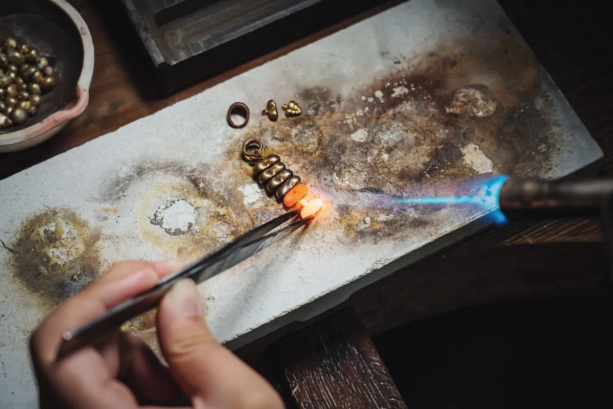 A skilled artisan uses a blowtorch and pliers to create handmade jewelry, highlighting craftsmanship in vintage jewelry.