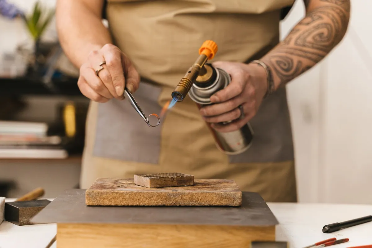 A jeweler uses a torch to craft a ring, highlighting artisanal skills amid changing gold prices.