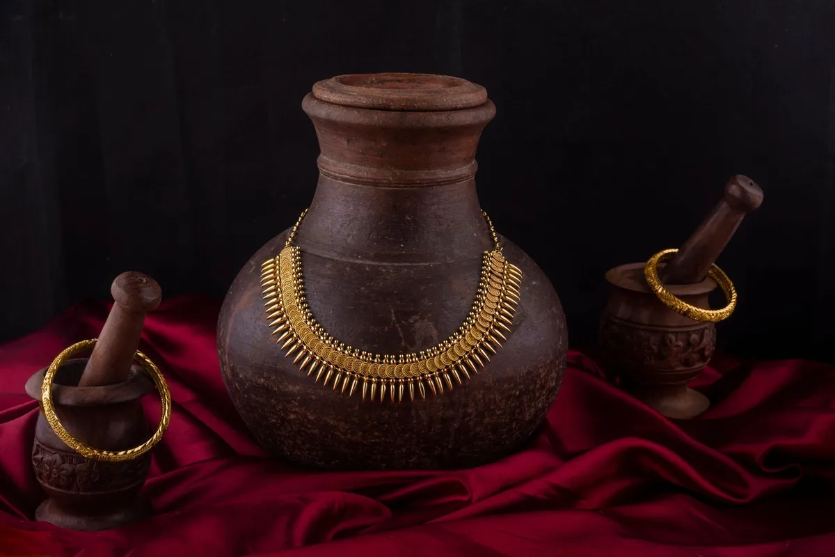 Traditional Indian necklace and bangles displayed on vintage pottery with a red fabric backdrop.