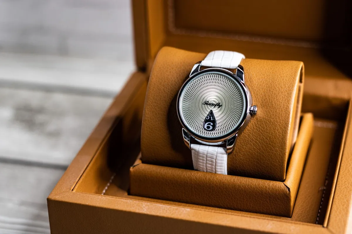 Close-up of a luxury watch with a white strap resting in a brown leather box, highlighting current trends.