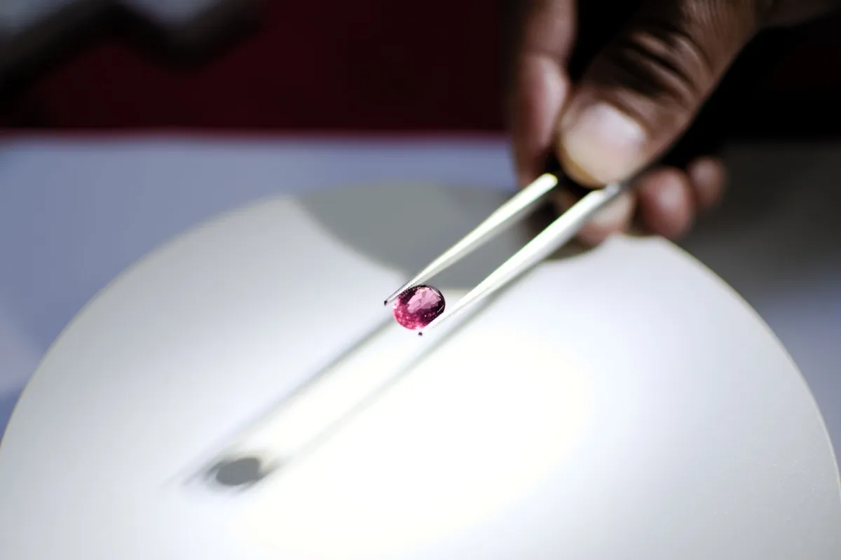 A hand holding a red gemstone with tweezers, highlighting the importance of gem evaluation in selling estate jewelry.